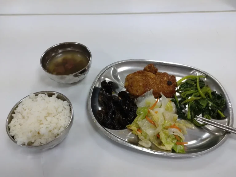 圖的左邊是一碗略滿的白飯，左上方有一碗紫菜湯，右邊則是餐盤。餐盤上有：一塊滷排骨，炒青菜、高麗菜和木耳。